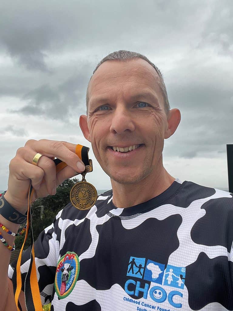 Foto von Axel Rittershaus, Ultra Marathon Läufer, der eine Medaille des Comrades Ultra Marathons von 2022 in den Händen hält